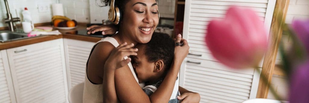 An affectionate mother embracing her young child in a warm, bright kitchen setting.