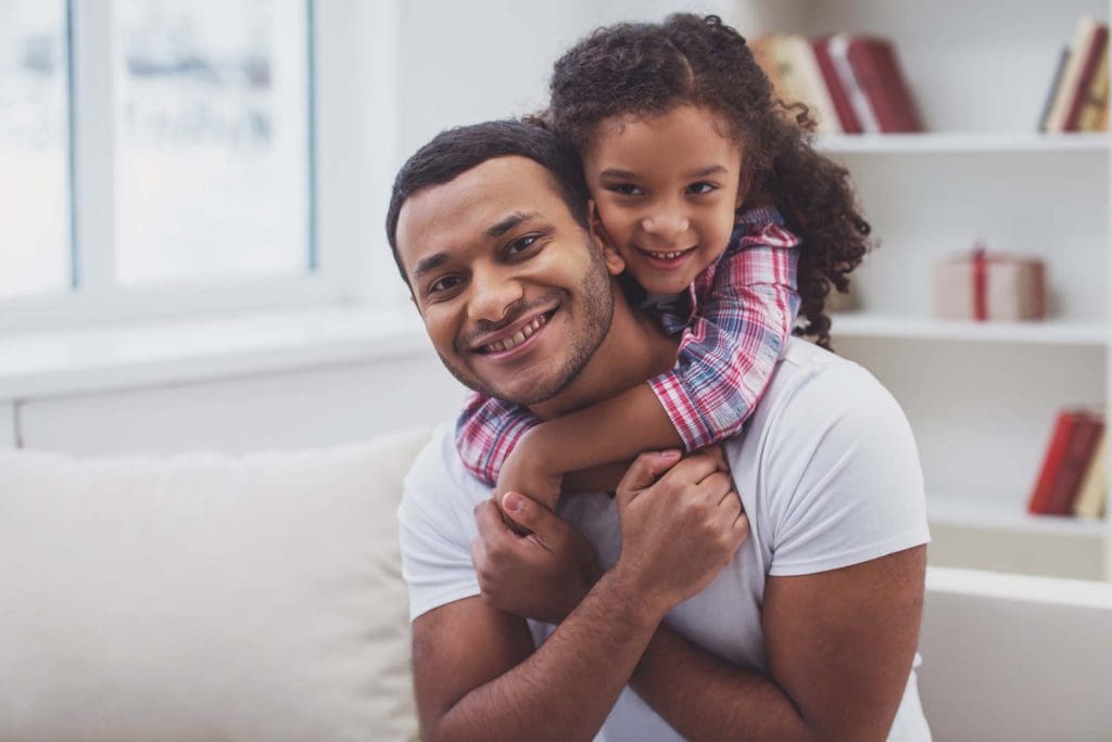 A happy father and his young daughter smiling together inside their secure home.