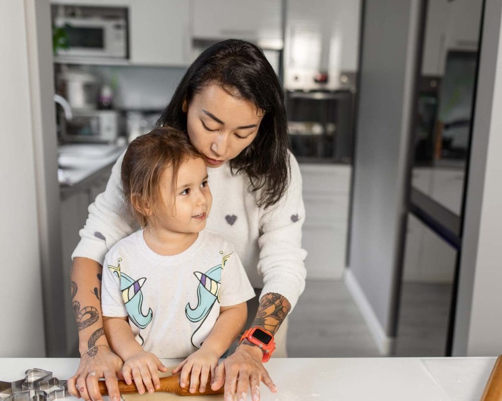 A mother and young child smiling and cooking together in a bright, modern kitchen.